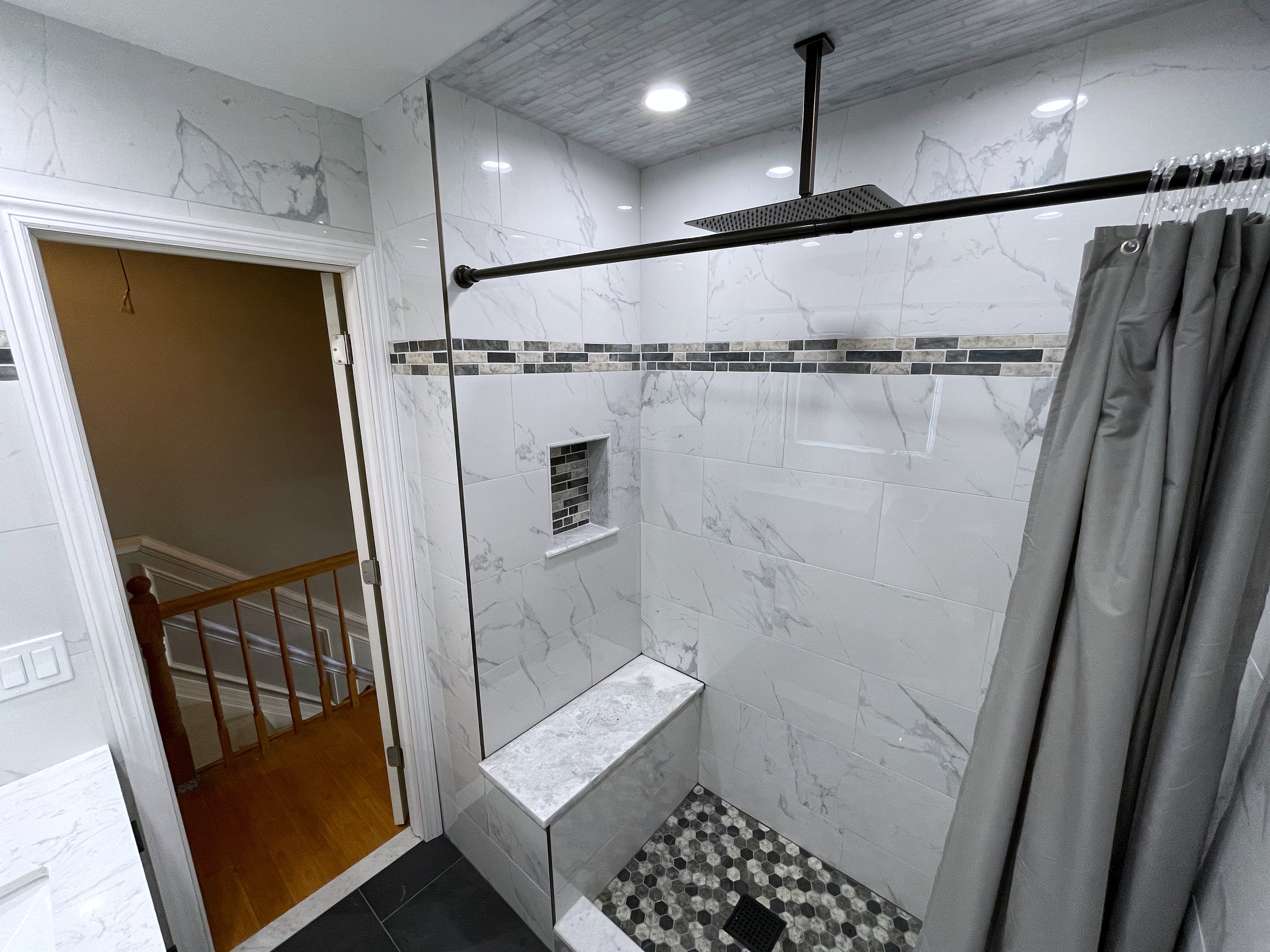 Tiled shower with bench, ceiling rain head, doorway to staircase